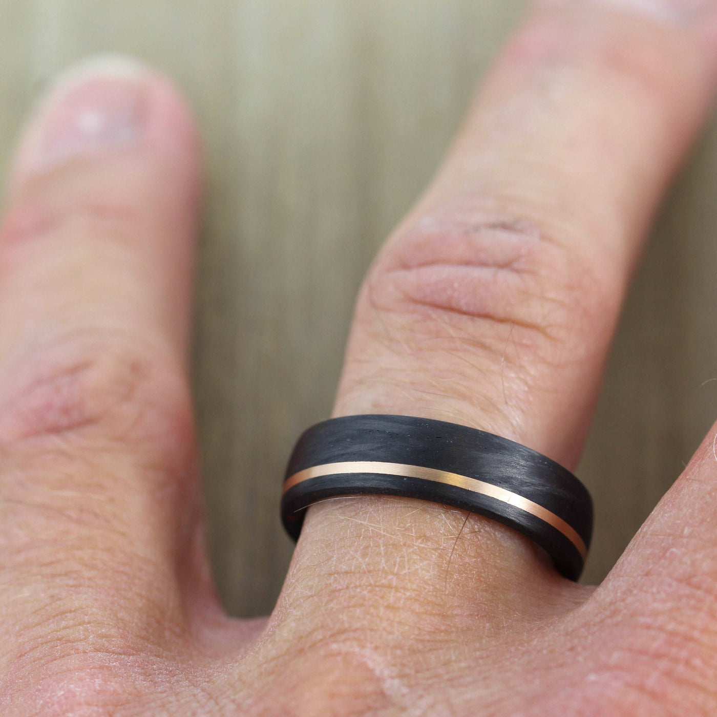 black carbon fibre wedding ring band. 6mm wide with a stripe of rose gold. black mans wedding ring uk