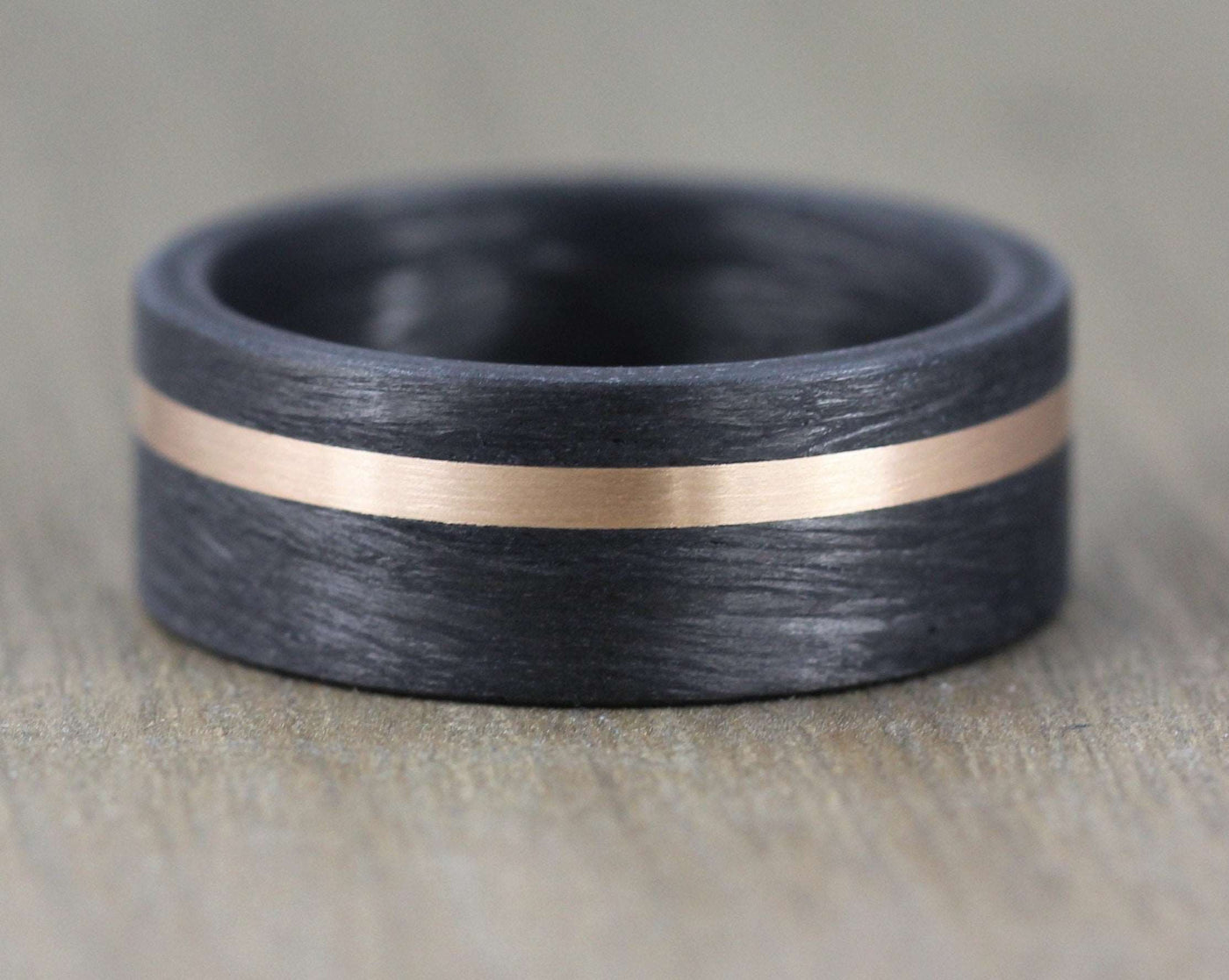 8mm Carbon Fibre wedding band with 2mm rose gold inlay. Comfort fit black carbon fibre wedding ring band. 8mm wide with a stripe of rose gold. black mans wedding ring uk
